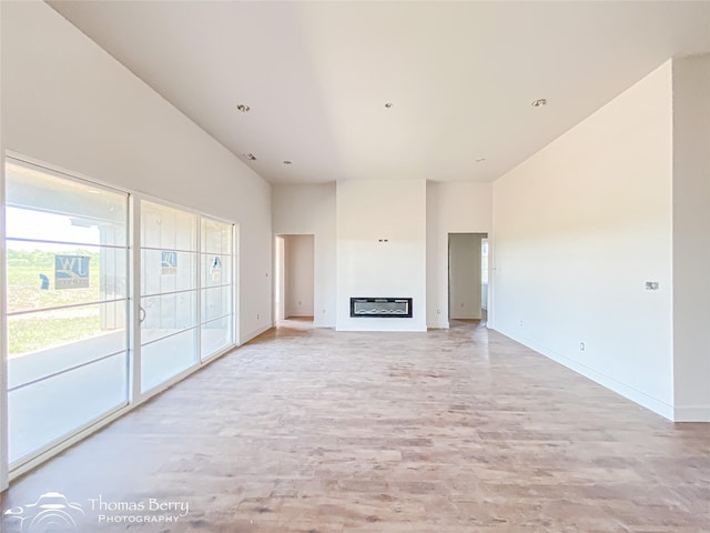 132 Pine Springs Cv, Tuscola, TX 79562 - unfurnished living room with light wood-style floors, high vaulted ceiling, baseboards, and a glass covered fireplace