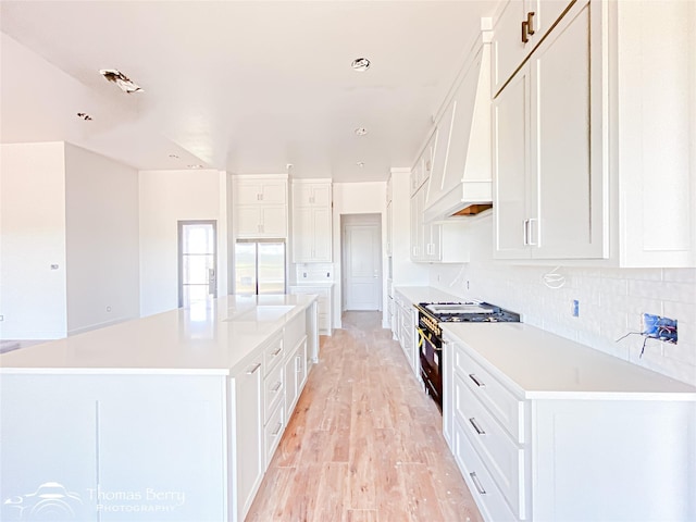 132 Pine Springs Cv, Tuscola, TX 79562 - kitchen with black gas range oven, light wood-style floors, a large island, backsplash, and white cabinetry