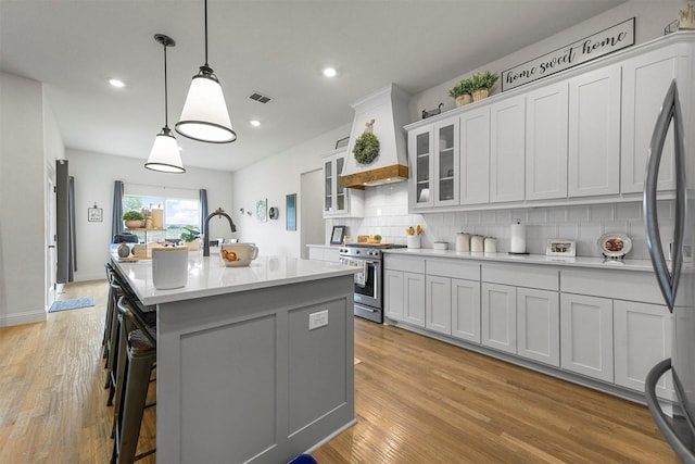 1511 Horseshoe Ct, Justin, TX 76247 - kitchen featuring high end stove, tasteful backsplash, an island with sink, light countertops, and light wood finished floors