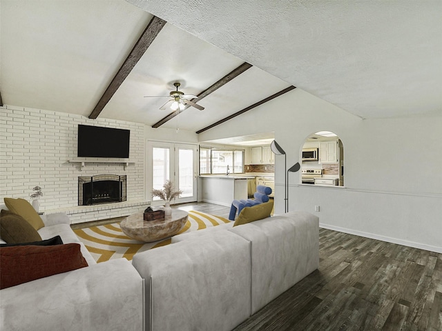 5632 Twitty St, The Colony, TX 75056 - living room with dark wood-style flooring, a ceiling fan, a fireplace, arched walkways, and baseboards