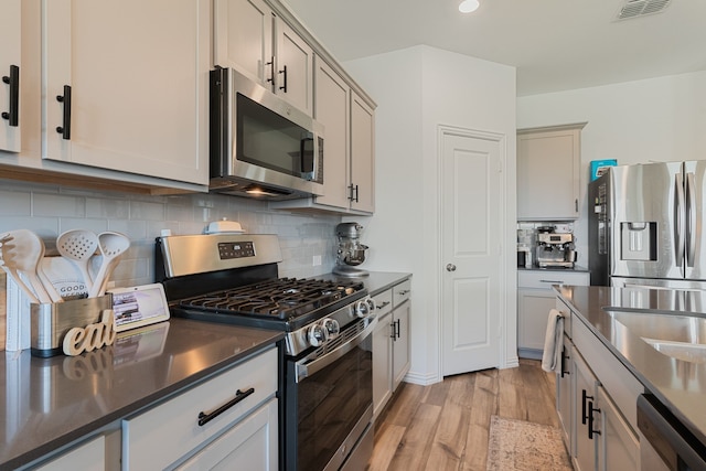 1701 Lake Grove Dr, Little Elm, TX 75068 - kitchen with stainless steel appliances, light wood-style floors, decorative backsplash, and dark countertops