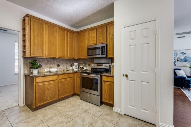 3717 Drew Dr, Frisco, TX 75035 - kitchen featuring appliances with stainless steel finishes, brown cabinetry, dark stone counters, and a textured ceiling