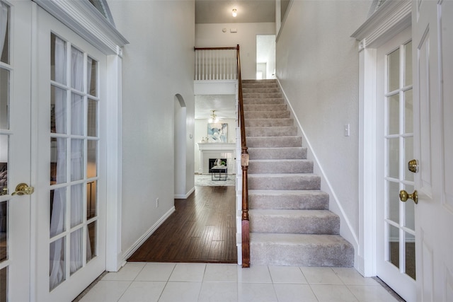 3717 Drew Dr, Frisco, TX 75035 - stairs with a fireplace with raised hearth, arched walkways, baseboards, tile patterned floors, and french doors