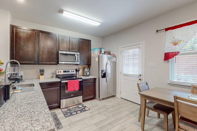 7448 Crossfire Trl, Fort Worth, TX 76112 - kitchen with stainless steel appliances, dark brown cabinets, light stone countertops, a sink, and light wood finished floors
