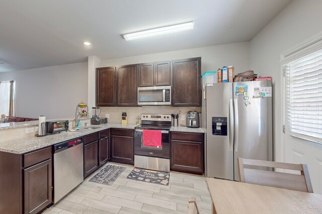 7448 Crossfire Trl, Fort Worth, TX 76112 - kitchen with appliances with stainless steel finishes, a sink, dark brown cabinets, a peninsula, and light stone counters