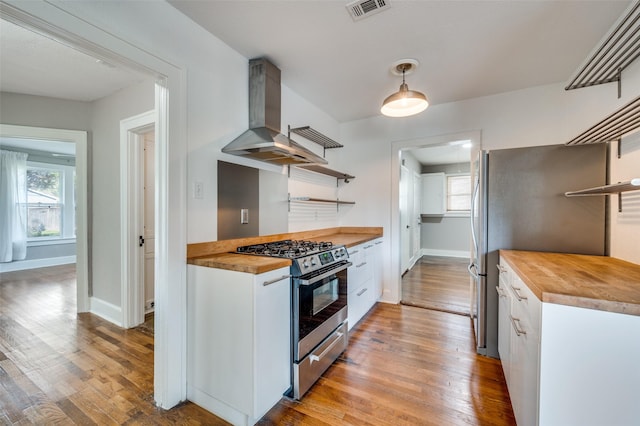 2615 W Brooklyn Ave, Dallas, TX 75211 - kitchen featuring open shelves, stainless steel appliances, butcher block counters, wall chimney range hood, and light wood-style floors