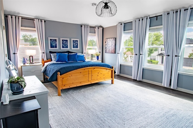 bedroom with multiple windows, a chandelier, wood finished floors, and baseboards