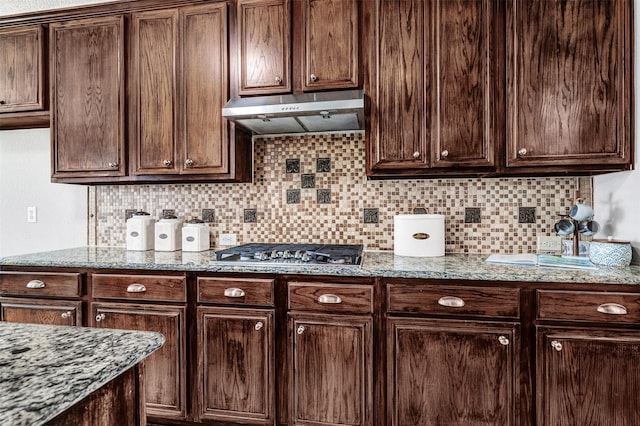 3501 Thorp Springs Dr, Plano, TX 75025 - kitchen with stainless steel gas cooktop, tasteful backsplash, dark brown cabinets, under cabinet range hood, and light stone countertops