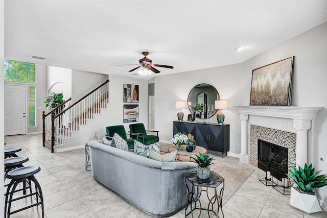 3501 Thorp Springs Dr, Plano, TX 75025 - living room with light tile patterned floors, ceiling fan, stairs, a tile fireplace, and a textured ceiling