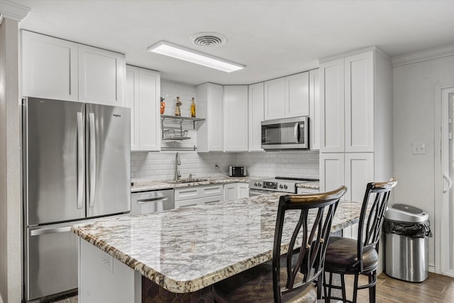 kitchen featuring stainless steel appliances, a sink, a kitchen bar, decorative backsplash, and dark wood-style flooring