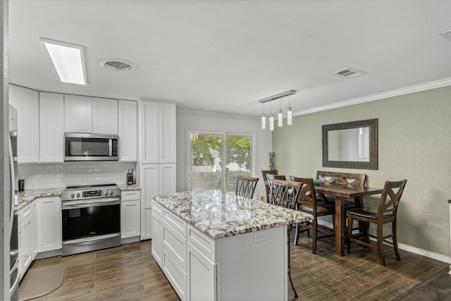 kitchen with appliances with stainless steel finishes, dark wood-style floors, ornamental molding, tasteful backsplash, and a kitchen island