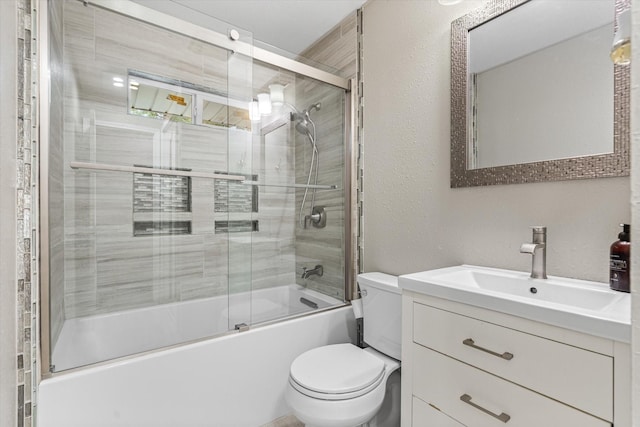 bathroom featuring toilet, a textured wall, bath / shower combo with glass door, and vanity