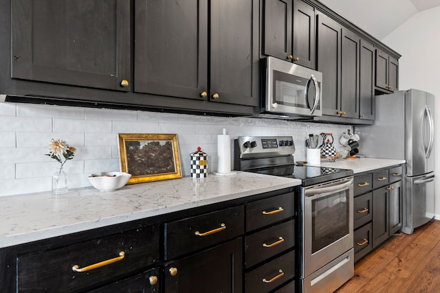 125 Singleton Dr, Royse City, TX 75189 - kitchen featuring stainless steel appliances, light wood finished floors, backsplash, dark cabinetry, and vaulted ceiling