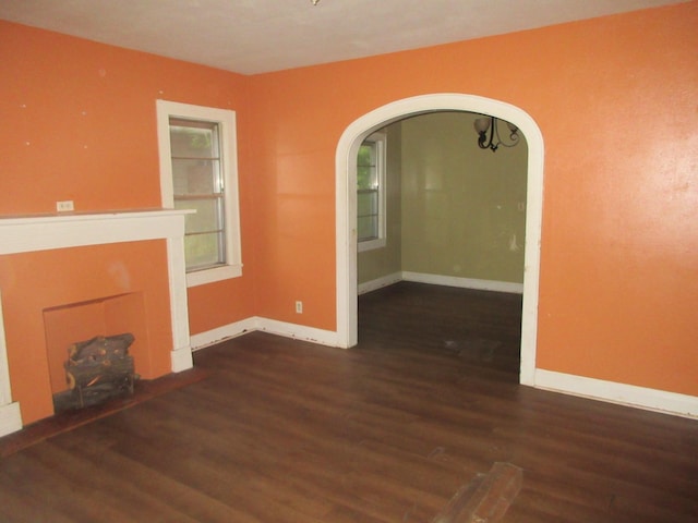 unfurnished living room featuring wood finished floors, arched walkways, and baseboards