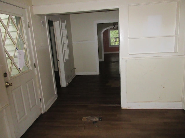 hallway with dark wood-style floors, arched walkways, and baseboards
