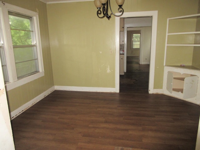 unfurnished dining area featuring a chandelier, dark wood-style flooring, crown molding, and baseboards