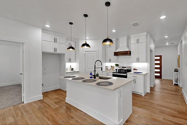 704 Witt, Wolfe City, TX 75496 - kitchen featuring stainless steel electric range, premium range hood, a center island with sink, light wood-style flooring, and white cabinets