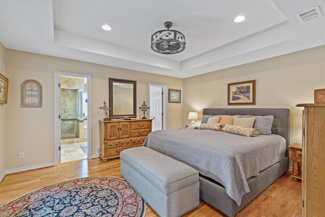 bedroom with a tray ceiling, light wood-style flooring, recessed lighting, baseboards, and ensuite bath