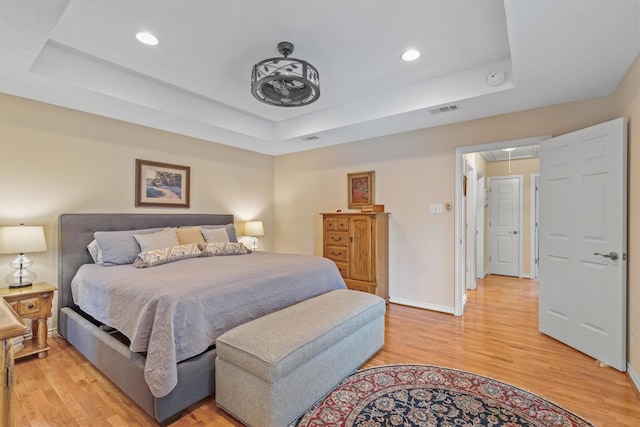 bedroom with attic access, a tray ceiling, light wood-type flooring, recessed lighting, and baseboards