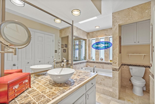 bathroom featuring a garden tub, vanity, tile patterned flooring, tile walls, and toilet