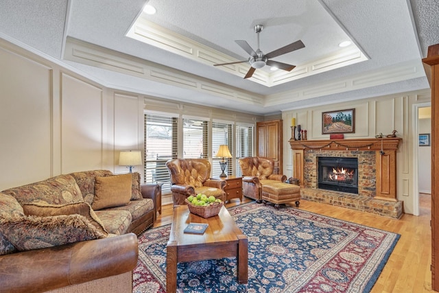 living room featuring a decorative wall, ceiling fan, light wood-type flooring, a textured ceiling, and a brick fireplace