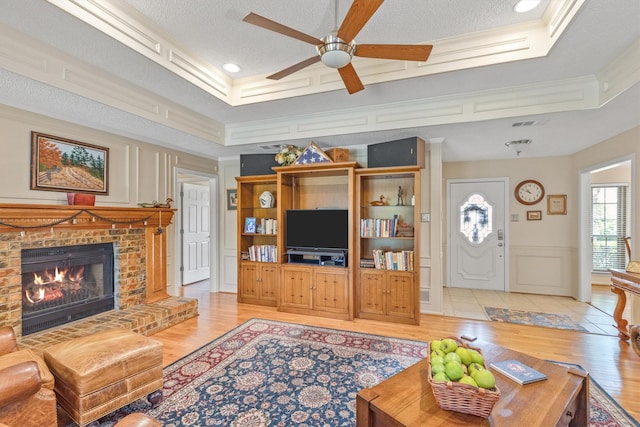 living room with crown molding, a decorative wall, ceiling fan, light wood-type flooring, and a fireplace