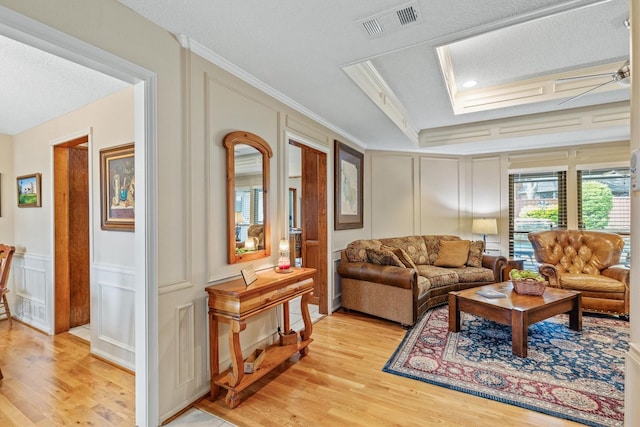 living area with a decorative wall, light wood finished floors, crown molding, and a textured ceiling