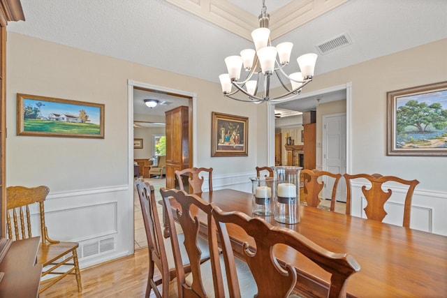 dining room featuring a chandelier, a decorative wall, a wainscoted wall, and light wood-style floors