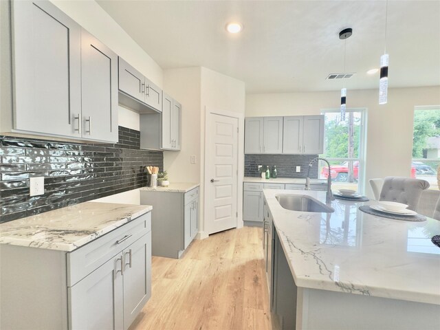 3801 Carpenter Ave, Dallas, TX 75210 - kitchen featuring a sink, light stone counters, decorative backsplash, light wood finished floors, and a center island with sink