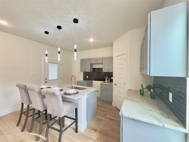 3801 Carpenter Ave, Dallas, TX 75210 - kitchen featuring gray cabinets, a sink, light wood-style flooring, tasteful backsplash, and an island with sink