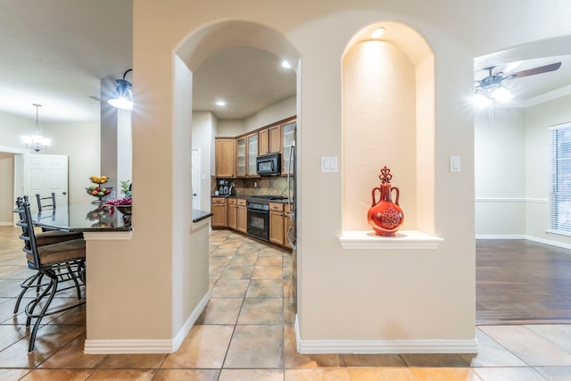 kitchen with black appliances, arched walkways, dark countertops, a kitchen bar, and tasteful backsplash