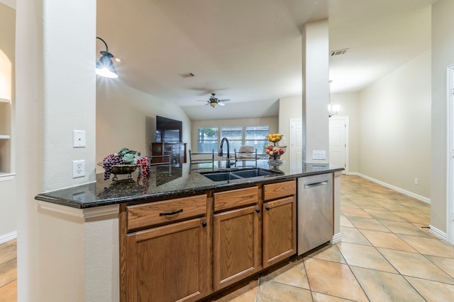 kitchen featuring dishwasher, a sink, ceiling fan, brown cabinetry, and dark stone counters