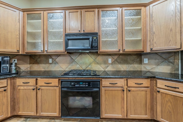 kitchen featuring black appliances, dark stone counters, glass insert cabinets, and backsplash
