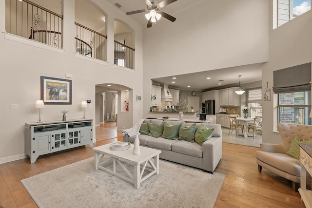 3002 Spring Hill Ln, Highland Village, TX 75077 - living room featuring arched walkways, ceiling fan, a towering ceiling, light wood-style flooring, and baseboards