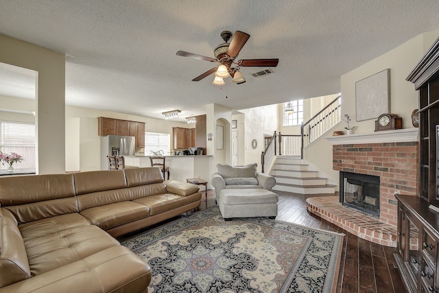 4205 English Ivy Dr, Mckinney, TX 75070 - living area featuring ceiling fan, a textured ceiling, dark wood-style floors, stairs, and a brick fireplace