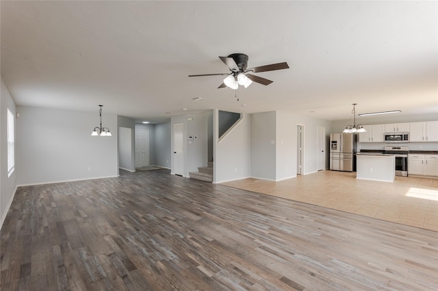 8537 Star Thistle Dr, Fort Worth, TX 76179 - unfurnished living room featuring a chandelier, light wood-style floors, ceiling fan, baseboards, and stairs