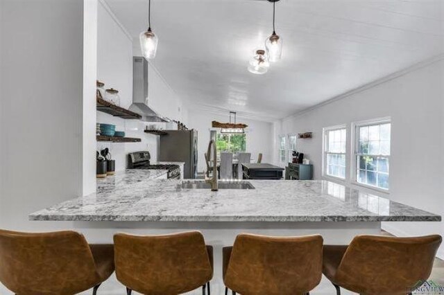 228 Stuart Dr, Karnack, TX 75661 - kitchen with stainless steel range oven, a sink, wall chimney range hood, a peninsula, and white cabinetry