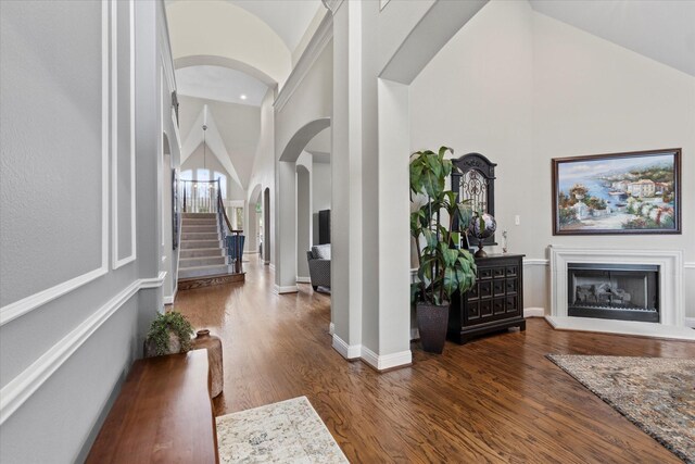 5581 Travis Dr, Frisco, TX 75034 - foyer featuring high vaulted ceiling, arched walkways, a fireplace with raised hearth, wood finished floors, and stairs