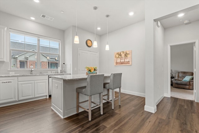 kitchen featuring dark wood finished floors, light stone countertops, white cabinets, a kitchen bar, and recessed lighting