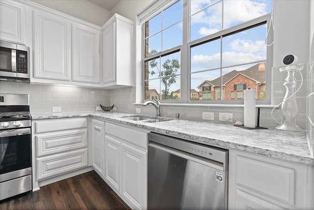 kitchen featuring appliances with stainless steel finishes, a sink, white cabinets, tasteful backsplash, and light stone countertops