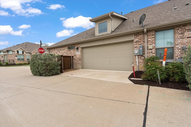view of side of property with concrete driveway, brick siding, an attached garage, and a shingled roof