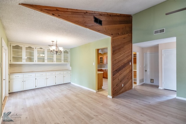 3242 Whitewing Way, Abilene, TX 79606 - unfurnished dining area with a chandelier, light wood-style floors, baseboards, wood walls, and a high ceiling