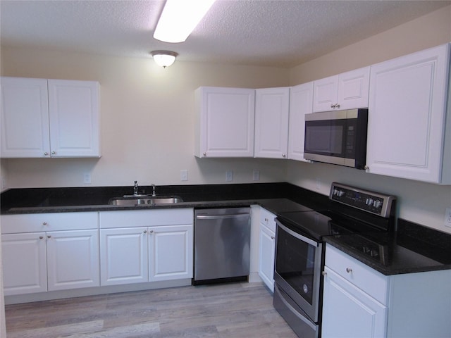 7928 Hull Ave, Dallas, TX 75216 - kitchen featuring stainless steel appliances, a sink, white cabinets, light wood finished floors, and a textured ceiling
