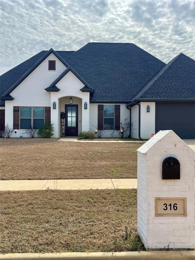 316 Heritage Way, Bullard, TX 75757 - french country style house featuring a shingled roof, an attached garage, and brick siding