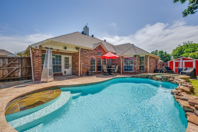 view of pool featuring a shed, a patio area, a fenced backyard, an outbuilding, and a pool with connected hot tub