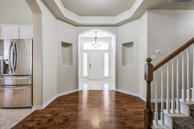foyer entrance with arched walkways, stairway, wood finished floors, and baseboards