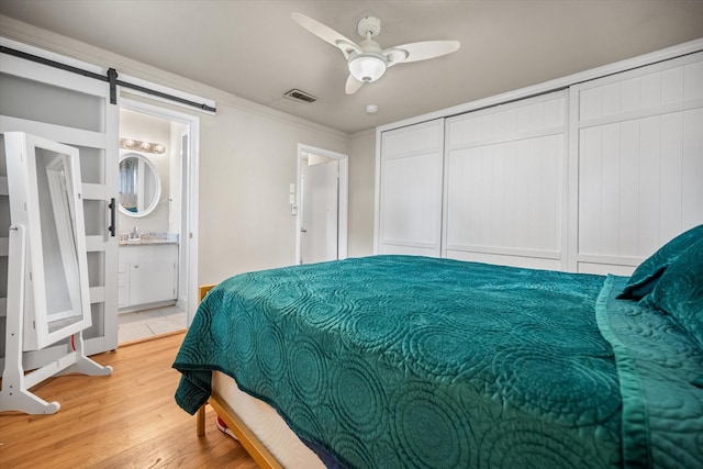 4900 Ira St, Haltom City, TX 76117 - bedroom featuring a barn door, crown molding, light wood-style flooring, a ceiling fan, and ensuite bath