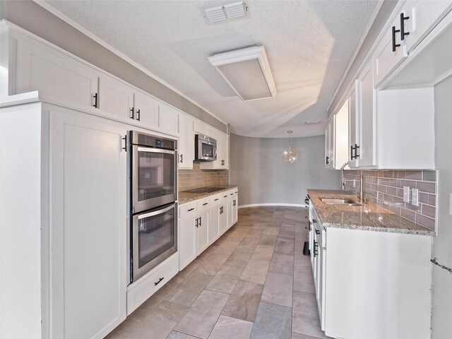 4509 Trowbridge Dr, Arlington, TX 76013 - kitchen with appliances with stainless steel finishes, a sink, tasteful backsplash, a textured ceiling, and white cabinets