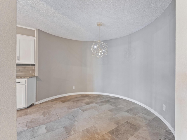 4509 Trowbridge Dr, Arlington, TX 76013 - unfurnished dining area featuring stone tile floors, a textured ceiling, and baseboards