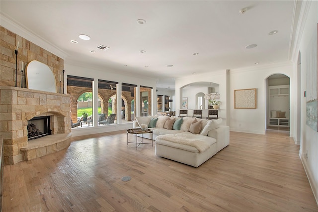 living area with crown molding, arched walkways, a fireplace, light wood-style floors, and baseboards